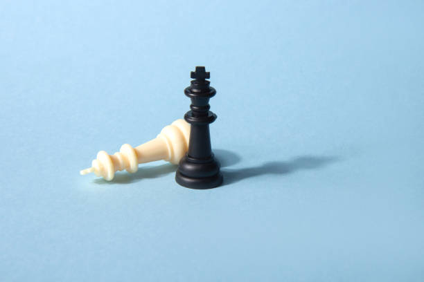 istock Two black and white king chess pieces on a blue background with one fallen. Abstract background 1370044461