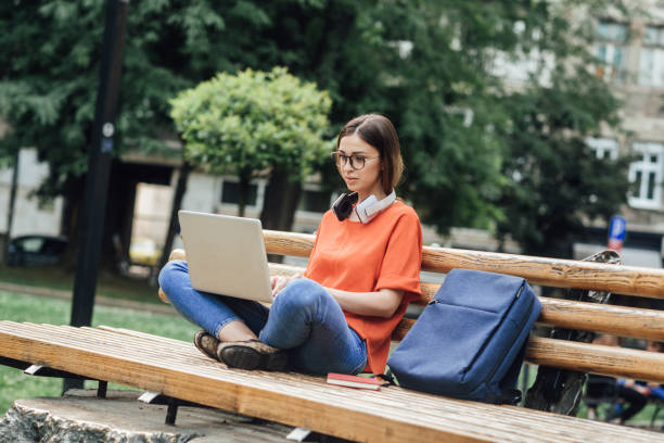 istock Girl sitting in the park and learning online 1370046280