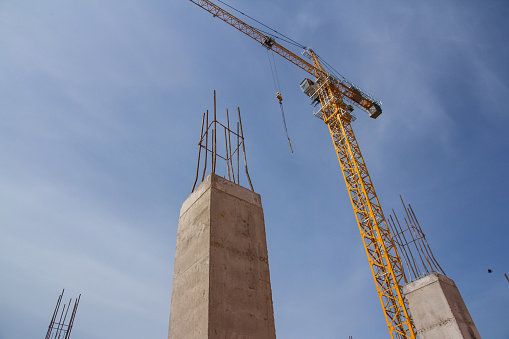 Reinforcement concrete column under construction at the construction site and tower crane against blue sky. construction site background