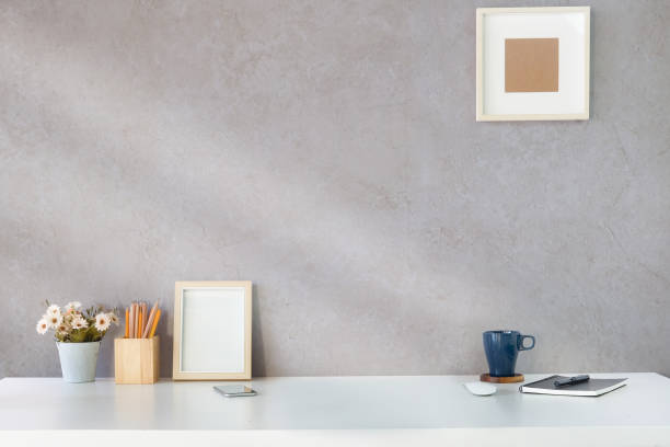 istock Stylish workplace with picture frame, notebook, pencil holder, flower pot and coffee cup on white table. 1370061203