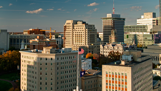 Aerial shot of office towers in Richmond, Virginia on a sunny afternoon in Fall, looking past the US and Virginia flags flying atop an office building towards the state capitol building.
