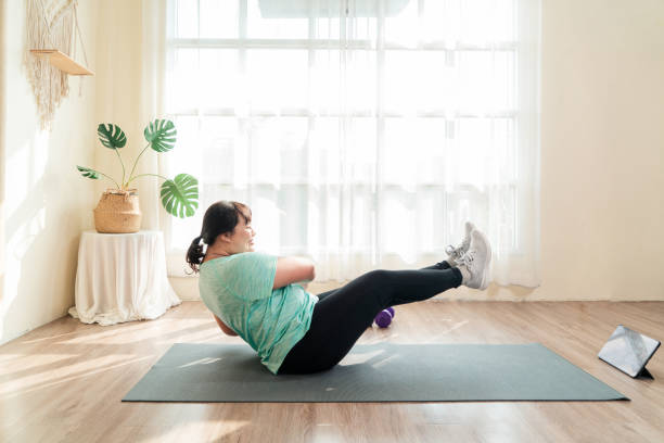Asian young female plus size in sport wear effort exercise training abdominal muscle on yoga mat in living room. stock photo