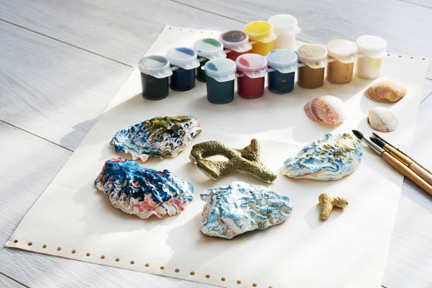 istock Child's craft place with shells have been painted different colors, paintbrushes and gouache paints. Child painting seashells for DIY project. 1370081052