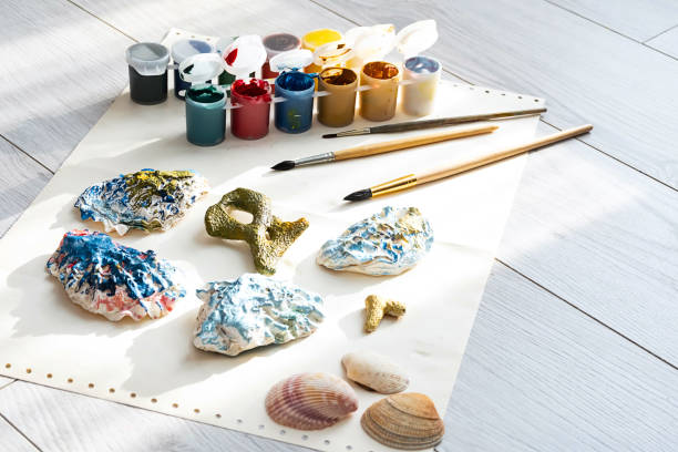 istock Child's craft place with shells have been painted different colors, paintbrushes and gouache paints. Child painting seashells for DIY project. 1370081054