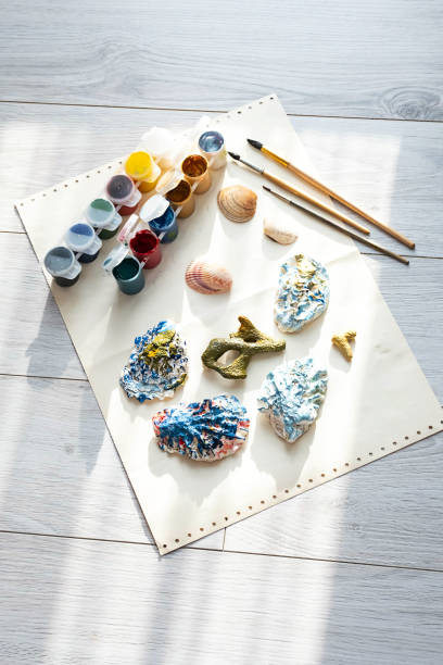 istock Child's craft place with shells have been painted different colors, paintbrushes and gouache paints. Child painting seashells for DIY project. 1370081057