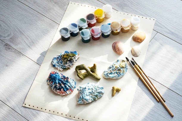 istock Child's craft place with shells have been painted different colors, paintbrushes and gouache paints. Child painting seashells for DIY project. 1370081058