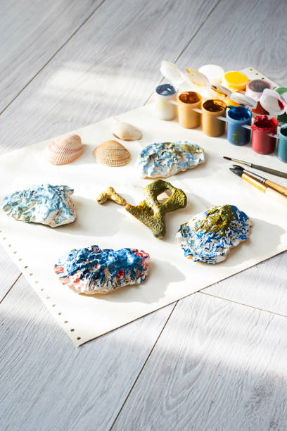 istock Child's craft place with shells have been painted different colors, paintbrushes and gouache paints. Child painting seashells for DIY project. 1370081064