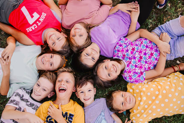 High angle view of a group of kids lying down while they laugh at the camera High angle view of a group of kids lying down while they laugh at the camera summer camp stock pictures, royalty-free photos & images