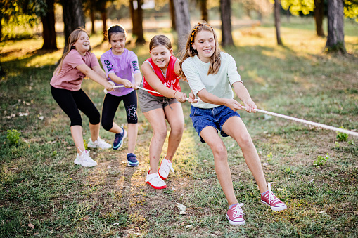 Large group of playful kids having fun in the park while playing tug-of-war.