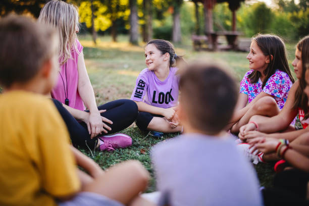 School children learning about ecology, nature and environment with teacher Children sit in a circle on the grass with the teacher and talk after sports activities travel9 stock pictures, royalty-free photos & images