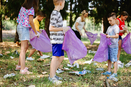 Large group of playful kids with garbage bags cleaning park. Ecology concept