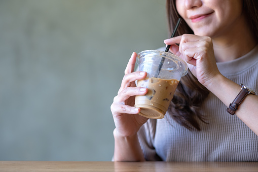 Closeup of a young woman holding and drinking iced coffee