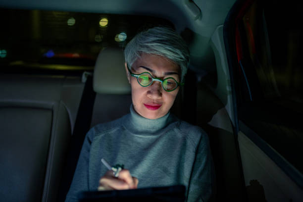 istock Senior woman using smartphone in the car under city lights 1370087849