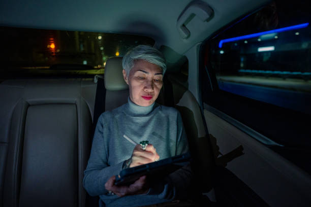 donna anziana che usa lo smartphone in macchina sotto le luci della città - taxi travel business women foto e immagini stock