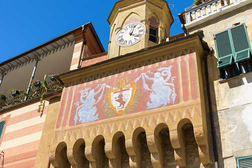 Finalborgo, Finale Ligure, Italy. May 5, 2021. Detail of the facade of the ancient Porta Testa with the coat of arms of Giovanni I del Carretto and the Bell Tower with Clock.