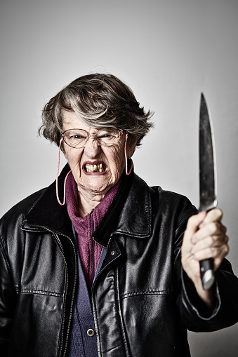 Woman in her 70s grimaces in fury, holding a long knife.
