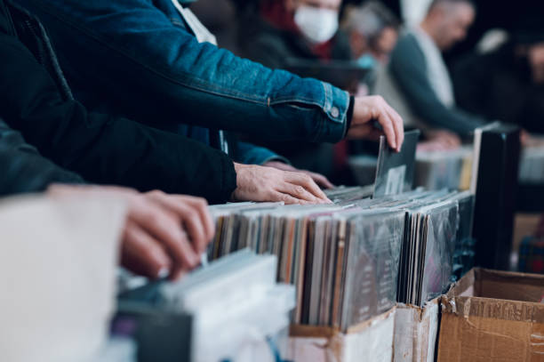 Close up of man browses through vinyl records in a retro-themed vintage store; Bright lighting highlights the vibrant red record he holds