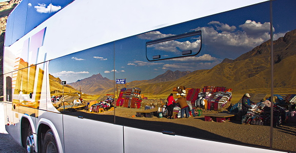 Abra La Raya, Andes , Peru - August 19,2019: Yellow Andes mountains are reflected on the windows of a tourist bus. On the foreground, the reflection of outdoors crafts people selling their goods. Abra la Raya is a high mountain pass at an elevation of 4.350m (14271ft) above the sea level.