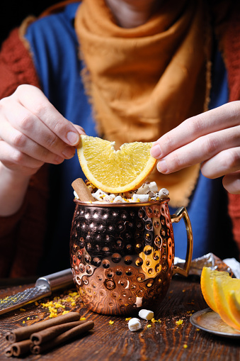 Woman is serving hot chocolate with marshmallows, orange and chocolate shavings in copper mug