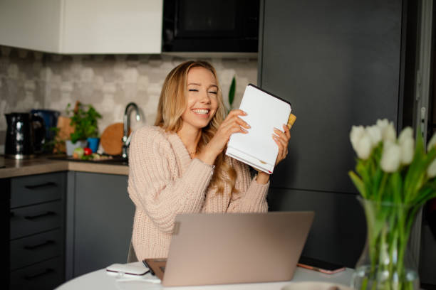 istock Smiling blond young woman with manuals and books studying online e-learning, using laptop at home. Online communication 1370101495