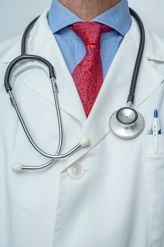 CLOSE UP OF THE TORSO OF AN ELEGANT DOCTOR WITH STETHOSCOPE, WHITE COAT, LIGHT BLUE SHIRT AND RED PRINTED TIE. TRUSTED DOCTOR AND HEALTH INSURANCE CONCEPT.