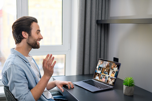 Caucasian man using laptop for video connection with friends. Man talking with young people on the screen. Video chatting concept. Stock photo