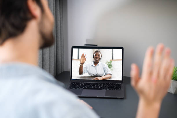 istock Cheerful carefree guy using laptop computer for video connection, looking at the webcam and waving hand. Man sitting at the table and making video call 1370106984