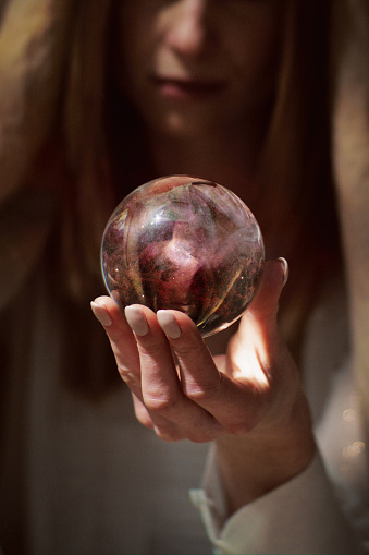 Woman fortune telling with glass sphere. Smiling and gesturing. Pink, digitally generated cosmic dust inside sphere
