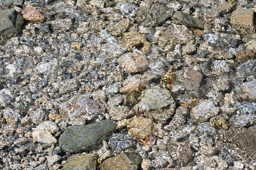 close-up of the texture of a crystal clear river bed with small stones in the background