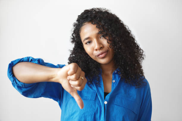 istock Negative human reaction, attitude and life perception. Serious displeased young dark skinned female with loose curly hair making thumbs down gesture, demonstrating her dislike and disrespect 1370114154
