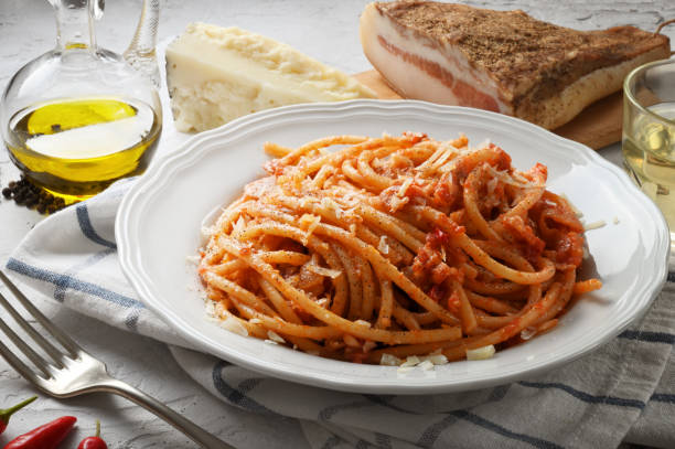 Amatriciana pasta. Bucatini amatriciana, famous Italian recipe from Amatrice. Basic ingredients on white plaster background, close-up. Spaghetti with peeled tomatoes, pecorino cheese, bacon, extra virgin olive oil, white wine, pepper and chilli. all'amatriciana stock pictures, royalty-free photos & images