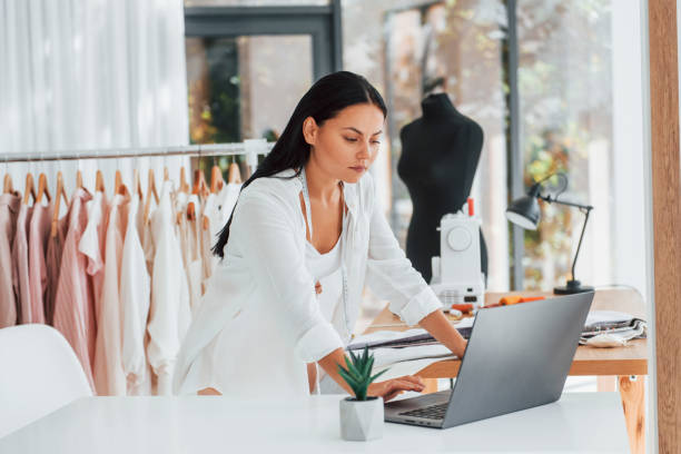 istock Using laptop. Seamstress is in her office that is with different clothes 1370118055