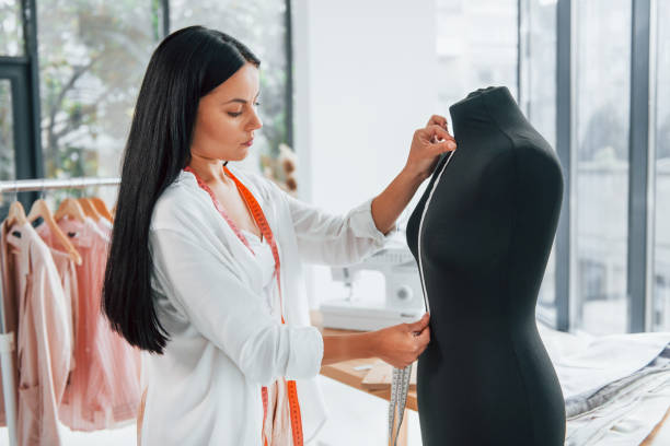 istock Using measuring tape. Seamstress is in her office that is with different clothes 1370118178