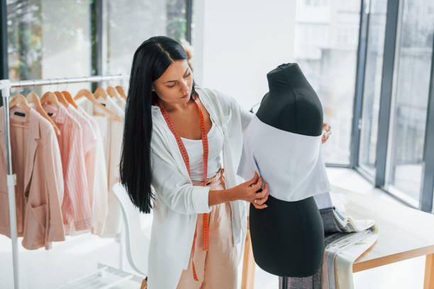 istock Using measuring tape. Seamstress is in her office that is with different clothes 1370118181