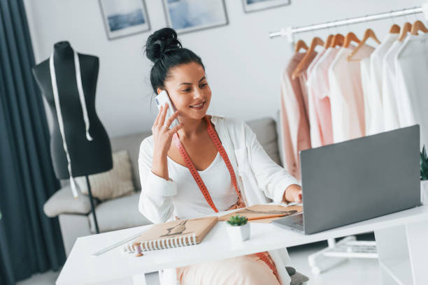 istock With laptop. Seamstress is in her office that is with different clothes 1370118334