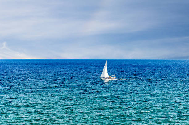 Scene of a small boat with sail in the middle of the blue ocean