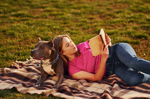 Lying down on a blanket. Woman in casual clothes is with pit bull outdoors.