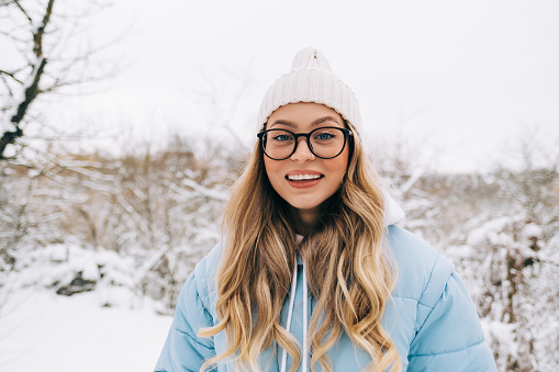 Portrait of attractive young woman standing in a winter park after snowfall.