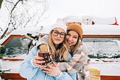 Portrait of two cheerful women friends heaving fun standing outdoor near van, enjoying winter time.
