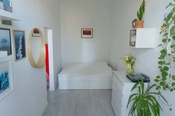 istock Bright white bedroom with bed, green plants, prints in frames and round mirror 1370125561