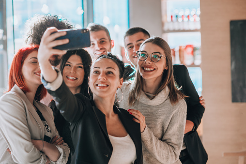Business partners in modern clothes taking group selfies at a café bar