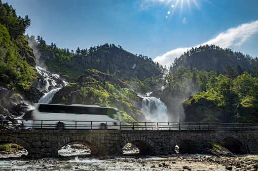 Tourist bus traveling on the road Latefossen Waterfall Odda Norway. Latefoss is a powerful, twin waterfall.