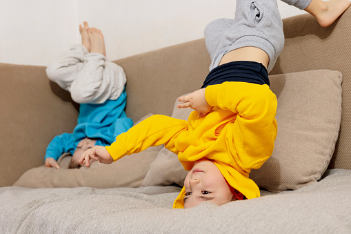 Two little caucasian kids doing gymnastic handstand exercise in living room. Children standing on hands upside down and having fun together. Sport at home. Workout in the apartment. Healthy lifestyle