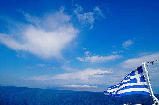 Greece, Aegean sea, Cyclades islands, travelling to Mykonos, Greek flag waving on a ferry boat.