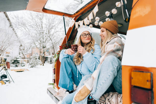Two cheerful women friends sitting in a van in winter camp and having fun, enjoying holiday. stock photo
