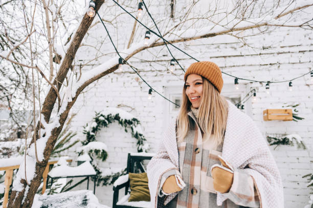 Portrait of young cheerful caucasian woman standing outdoor in the backyard after snowfall, enjoying winter time. stock photo