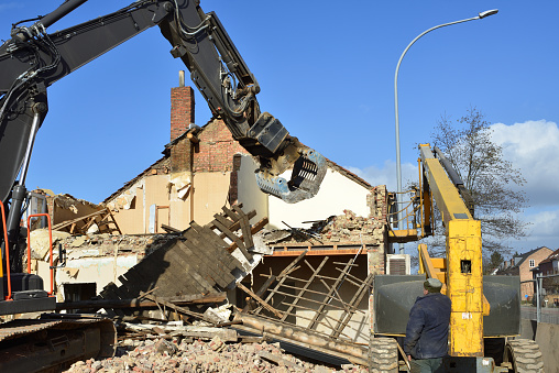House dismantled by a bulldozer. Rubble brick pulled down by a bulldozer on a sunny winter day. Grab crane in action