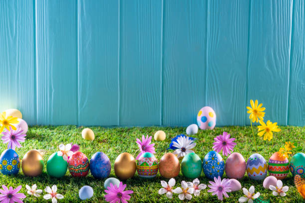 istock Easter eggs on turf grass and blue wooden wall with spring flowers 1370148853