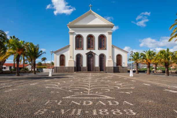 Beautiful old church in Funcal Madeira with a blue sky in background and a paved courtyard with text in foreground.