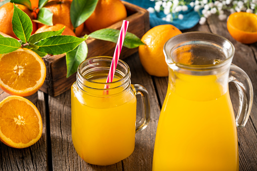 Orange juice in glass and carafe with fresh oranges on wooden table with nature background